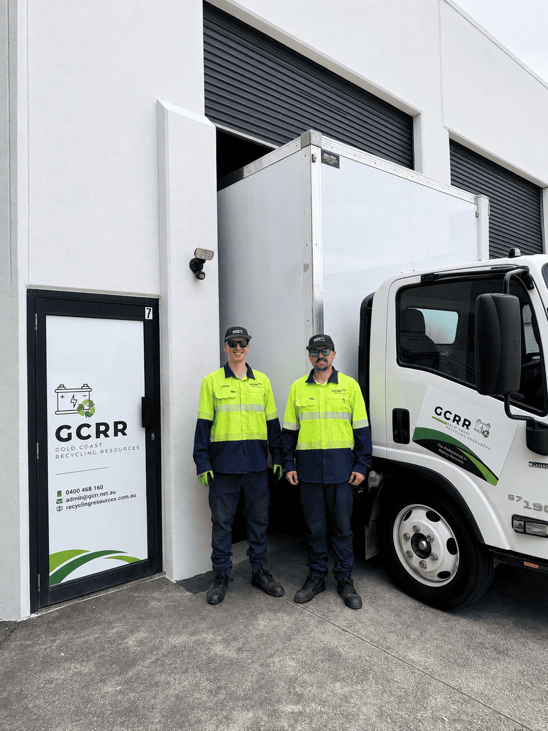 Team members Lance and Callum in high-visibility uniforms standing outside the Gold Coast Recycling Resources facility next to a branded commercial transport truck.   